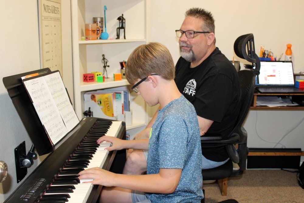 Older male watching as younger male plays a digital piano. 