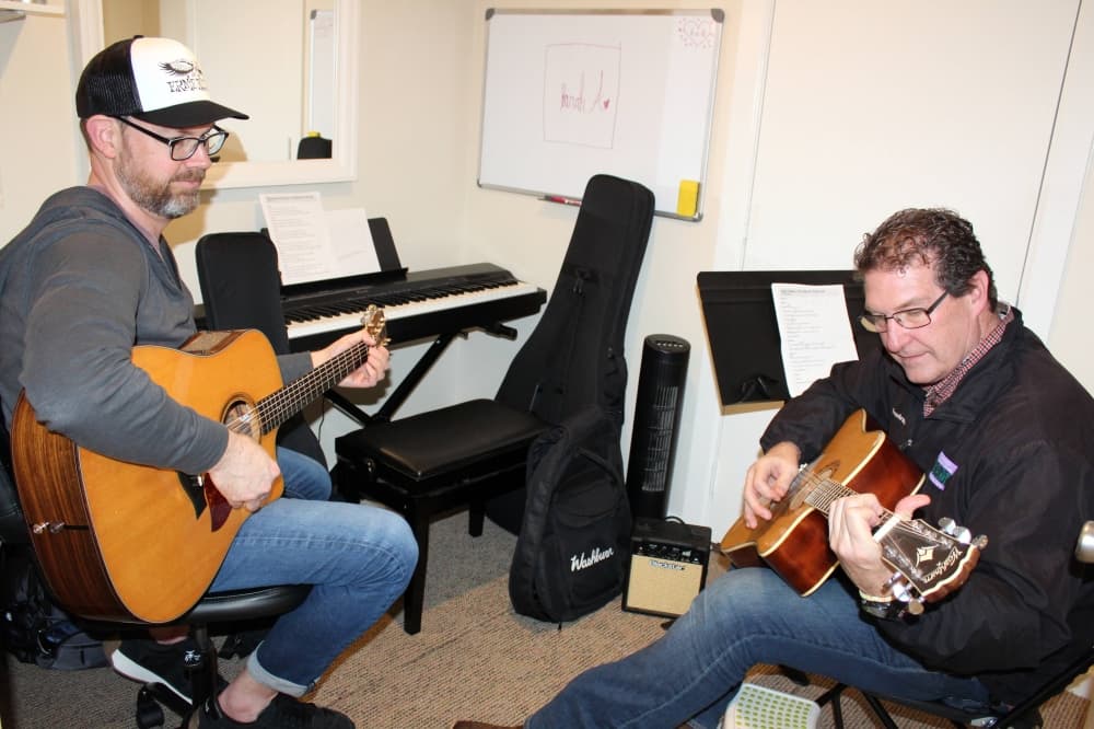 Two males playing guitar across from each other. 