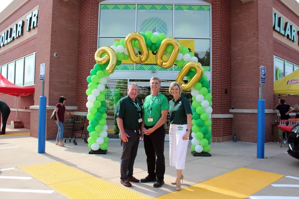 Two males and one female standing in front of a balloon arch in front of a Dollar Tree store. 