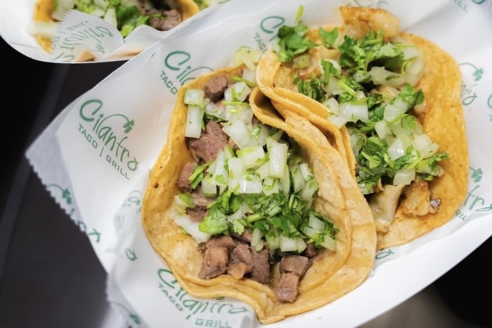 Overview of two tacos with meat, lettuce and cilantro. 