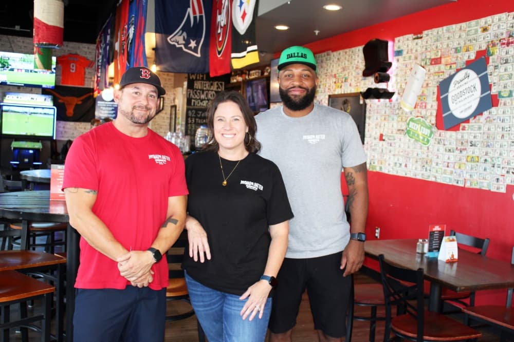 One female standing between two males in a bar. 