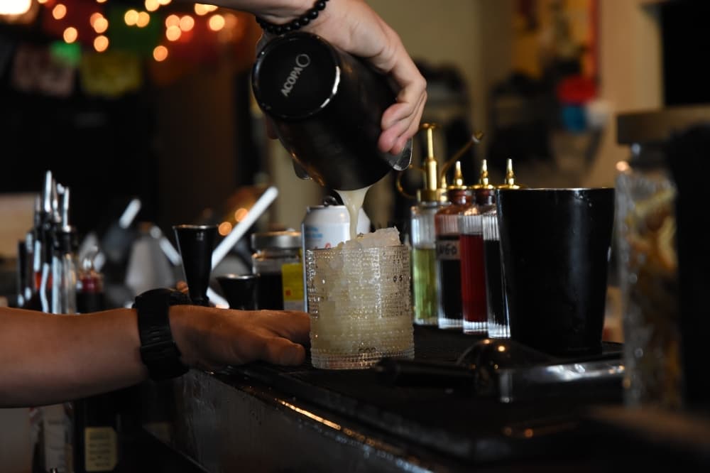 hands pour a cocktail into a glass from a shaker. 