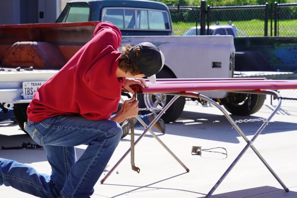 Student adds finishing touches to a car part after giving it a fresh paint job