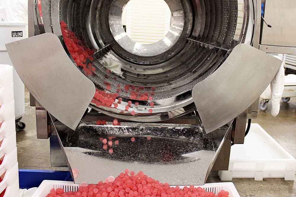 Pink gummies flowing from circular machine to catch tray. 