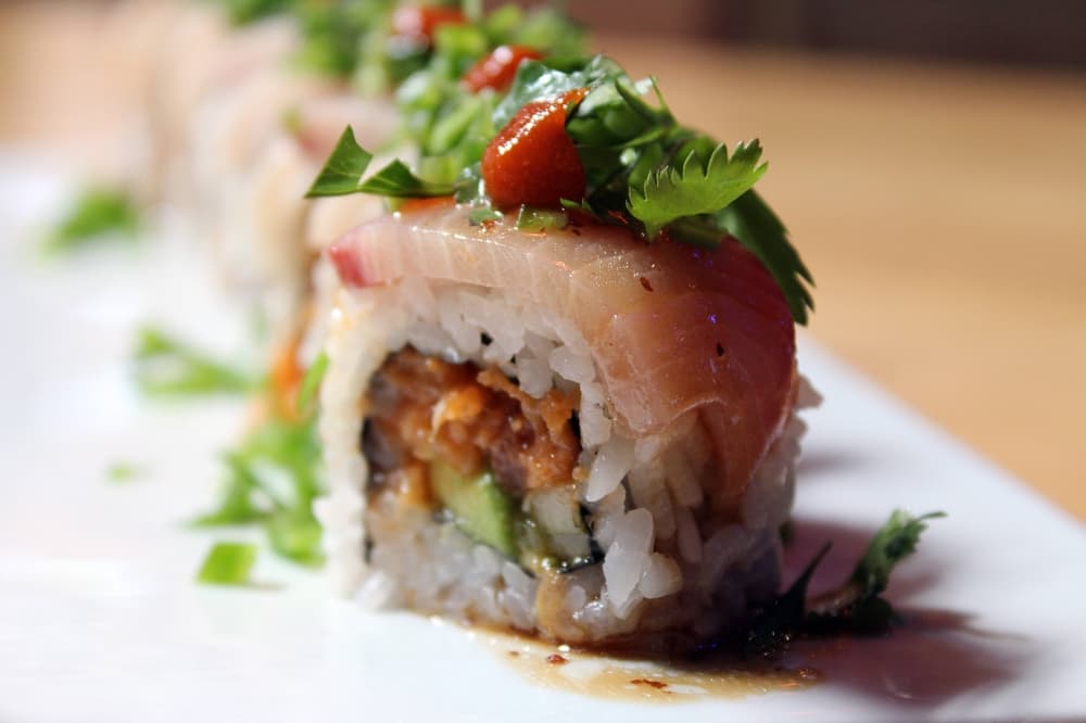 Sushi roll topped with sashimi and seasonings. 