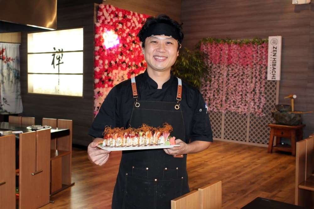 Male holding a plate of sushi in an Asian restaurant. 