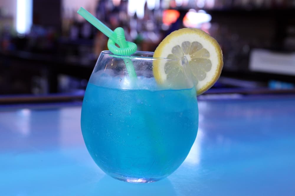 Blue cocktail garnished with a slice of lemon. 