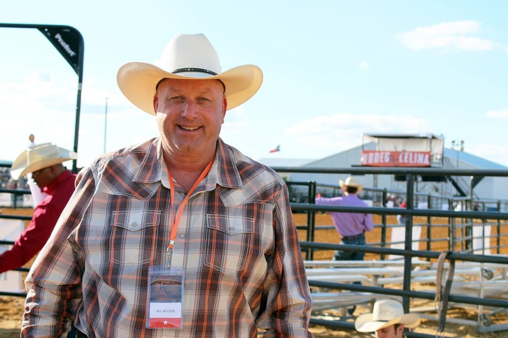 Male wearing a cowboy hat standing in front of an outdoor arena with Rodeo Celina banner in the background. 