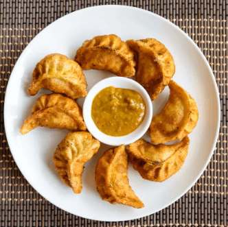 A plate of dumpling momos with a small bowl of dipping sauce in the center