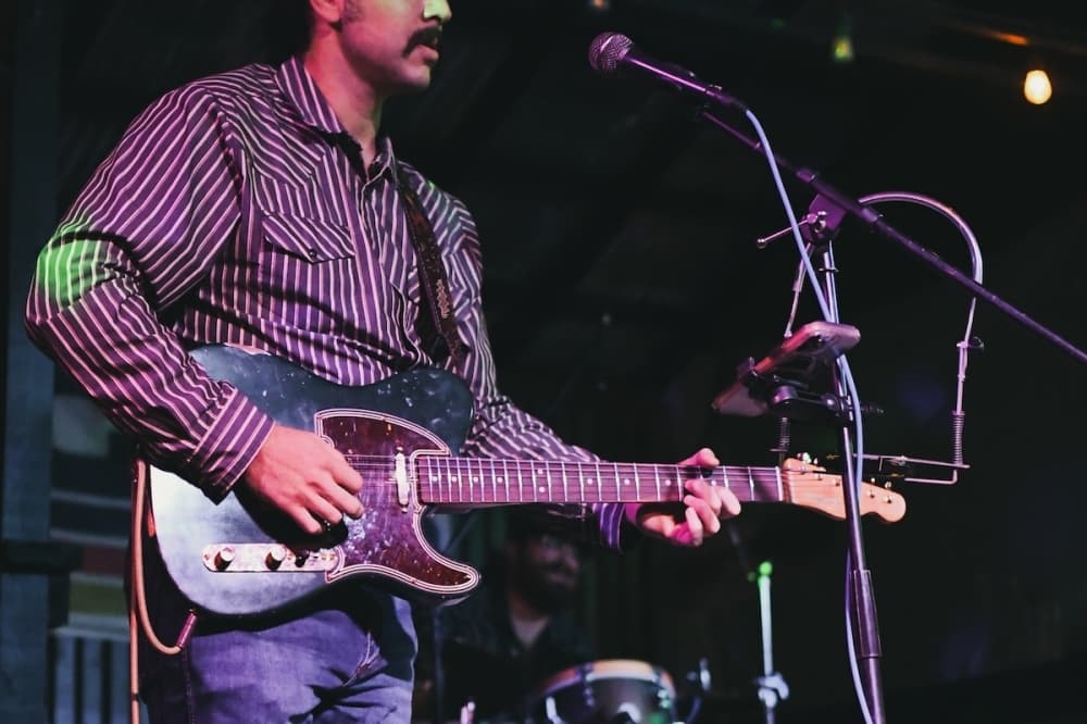 A guitarist performing onstage at an indoor concert venue.
