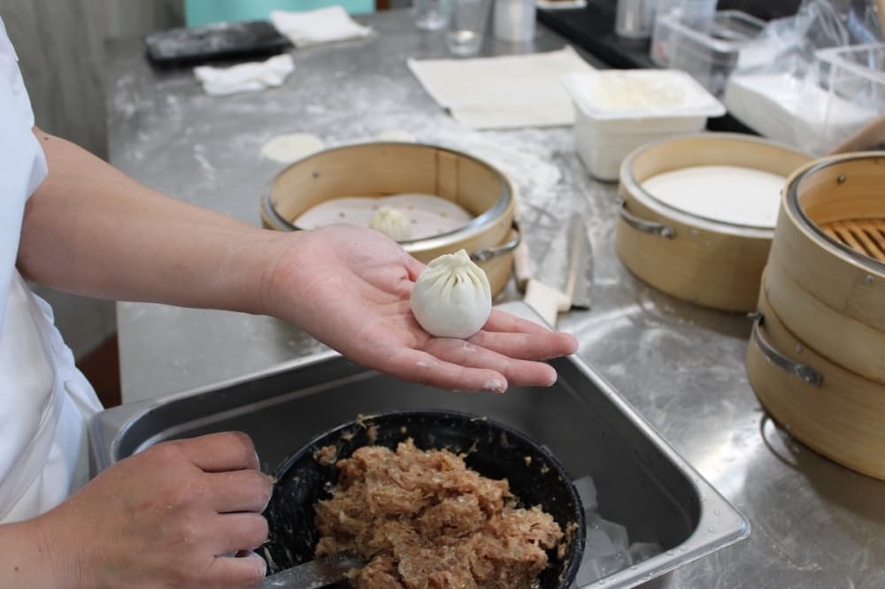 A chef holds a freshly made dumpling in her hand above her workstation.
