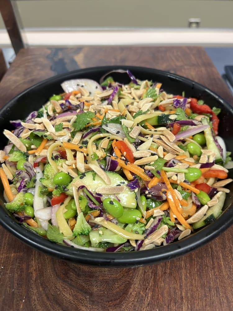 A black ceramic bowl with a brightly colored salad. Green edamame, red peppers, and orange carrots. 