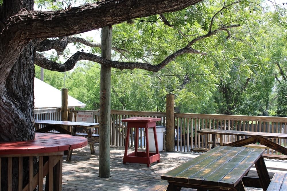 A porch shaded by a large oak tree with picnic tables and dining areas.