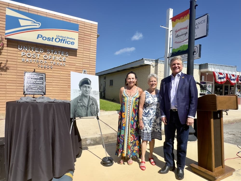 The two women are shown standing next to McCaul adjacent to a large photo of Billy Waugh and the plaque outside the post office.