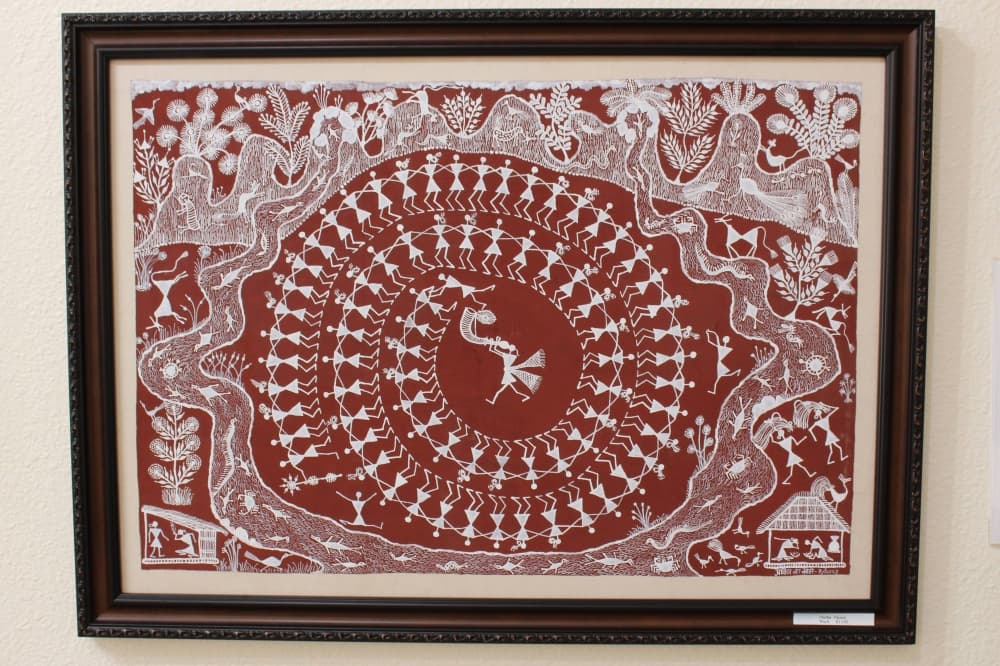Intricate white drawing of people walking in a spiral on a red canvas. 
