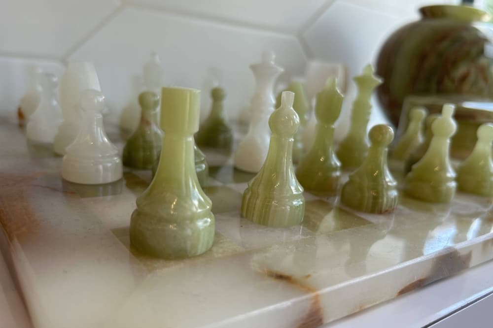Green and white marble chess pieces on a white marble chess board. 