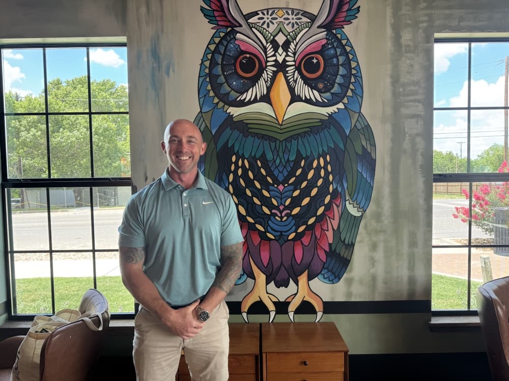 A man standing in front of a mural of an owl. 