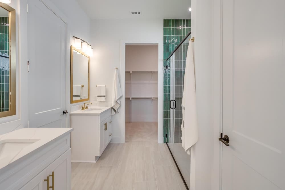 Stylish bathroom in El Paso II Ten Mile Creek model home with dual vanities and tiled walk-in shower. 