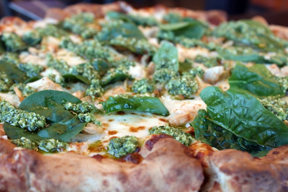 Pizza topped with pesto, spinach and Alfredo sauce. 