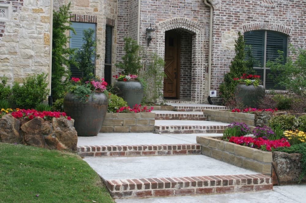 Exterior of a house with emphasis on flower beds and urns featuring seasonal flowers. 