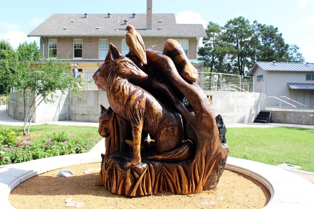Wooden 360-degree sculpture featuring a variety of wild animals displayed in front of a house. 