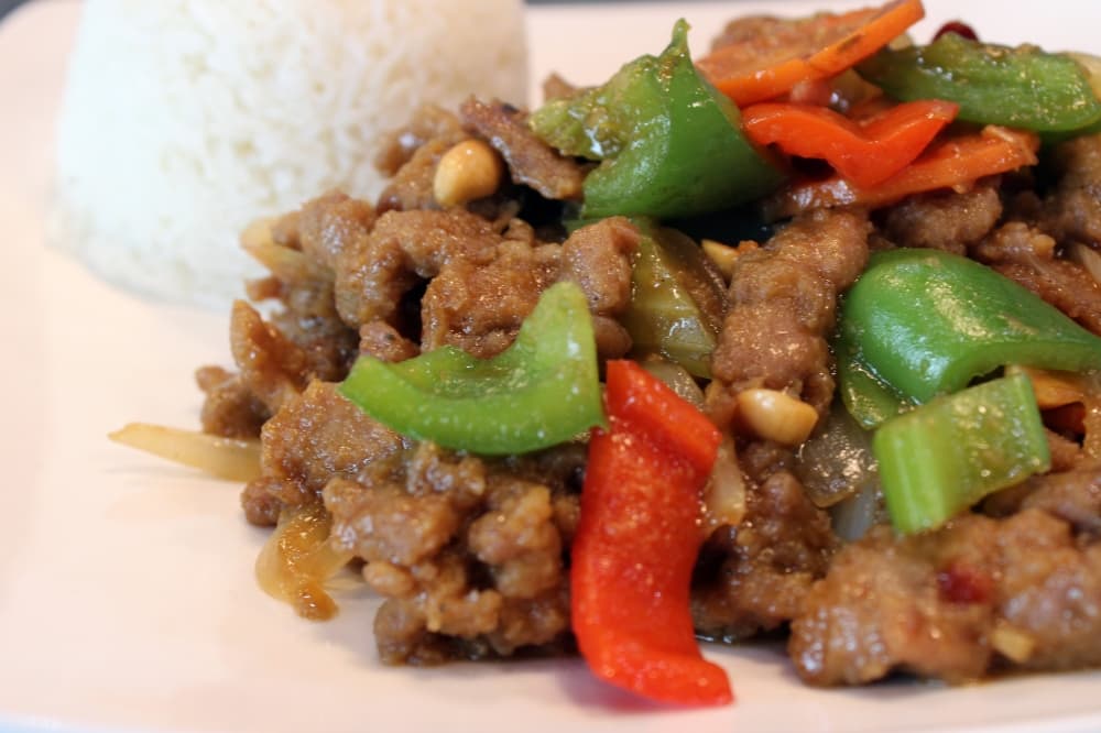 Dish of meat covered in sauce with peppers and side of rice. 