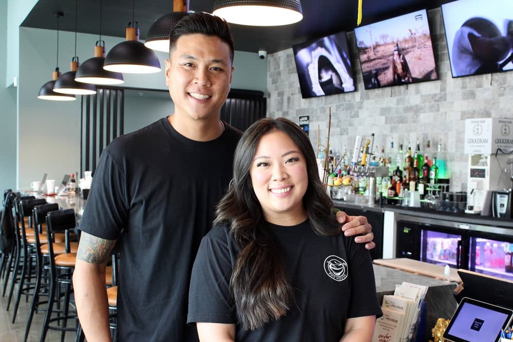 Adult male and female standing beside each other in front of a bar. 