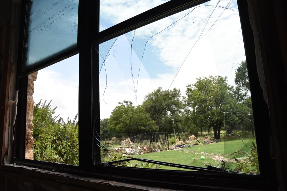 Debris is seen through a broken window. The debris is in the yard. 