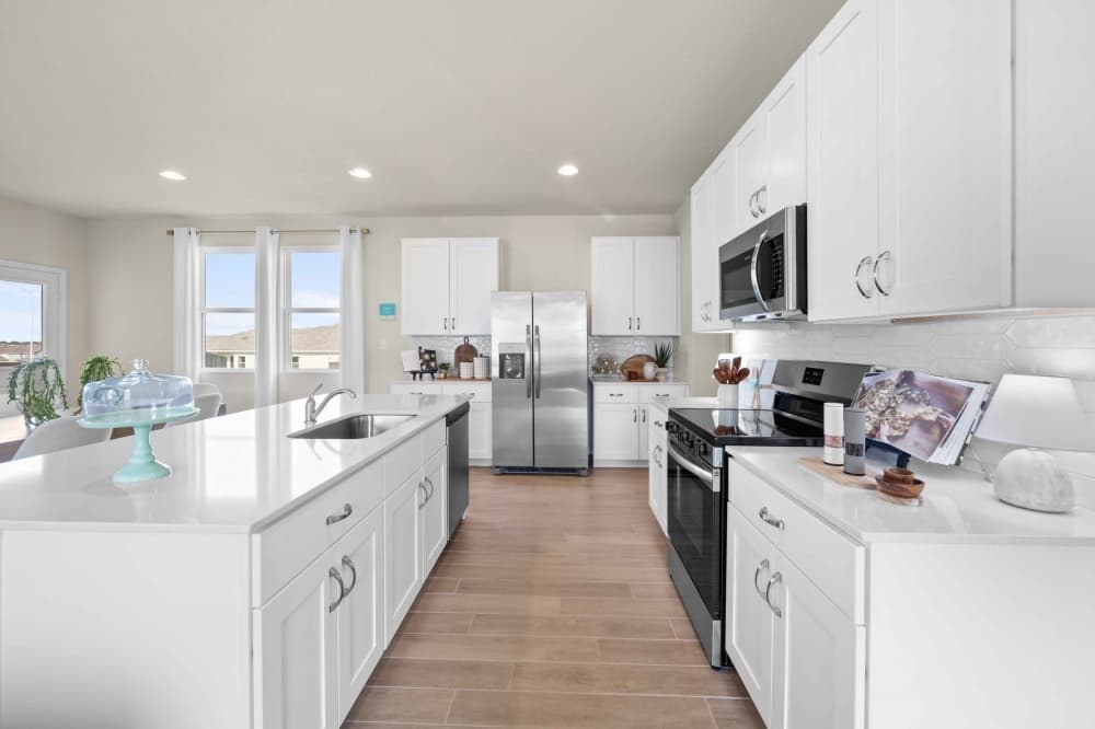 Modern Brohn Homes kitchen featuring white shaker cabinets, stainless steel appliances, a large island with quartz countertops, and natural light from oversized windows.