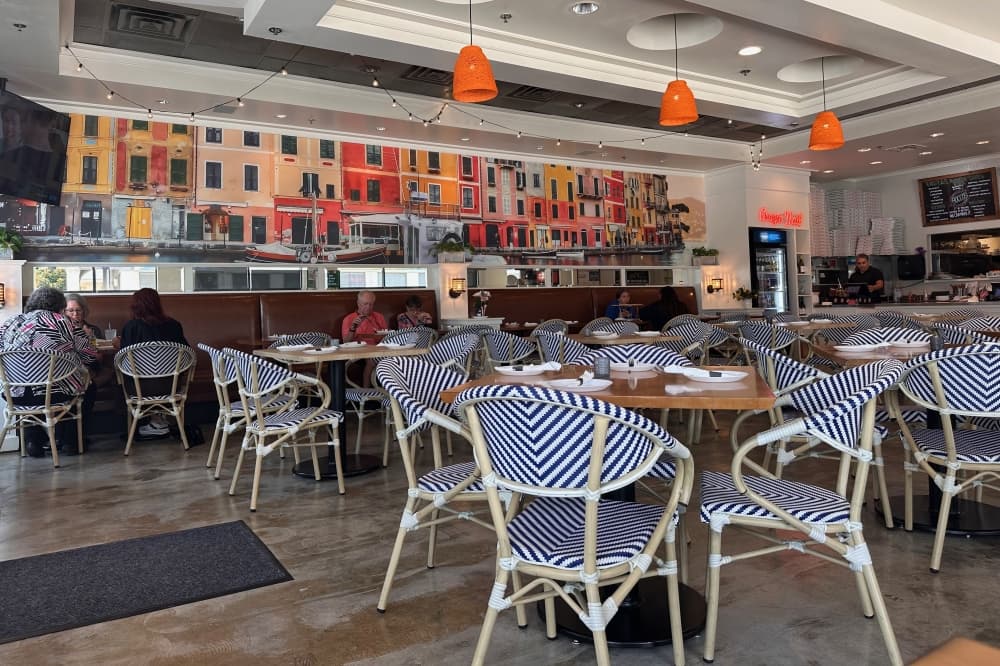 Dining tables and a painting on a wall of colorful buildings