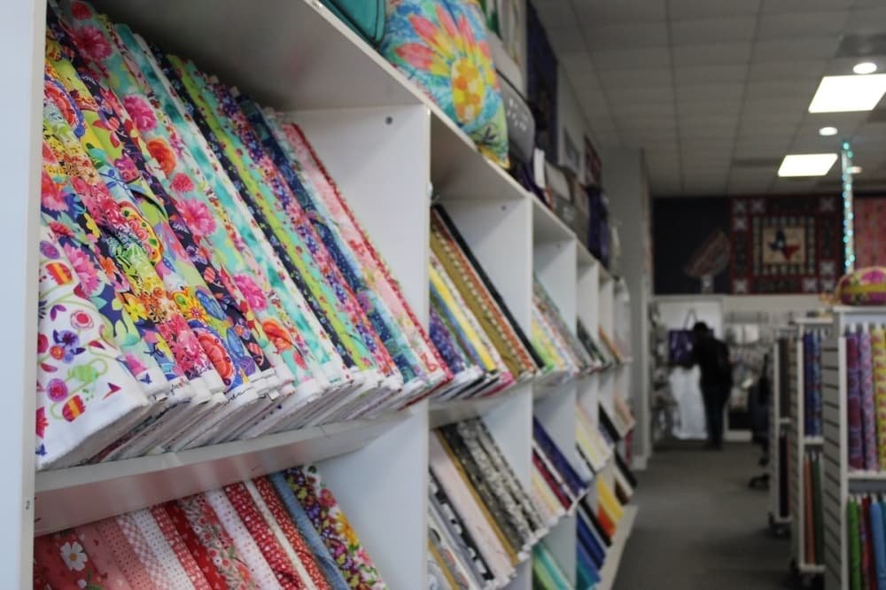 Shelves of multicolored and patterned quilting material ready to be stitched on sewing machines.