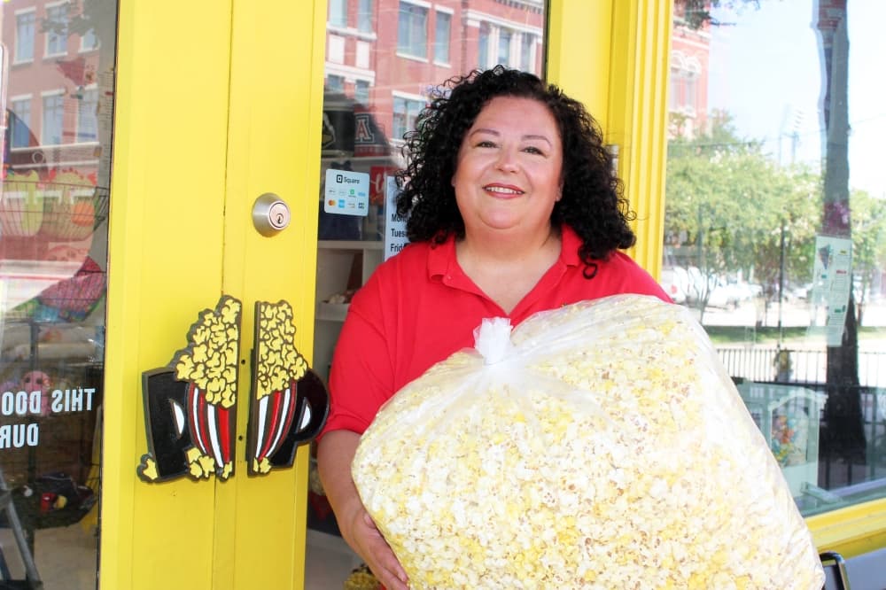Female holding an oversized bag of popcorn in front of a store with popcorn bags as door handles. 