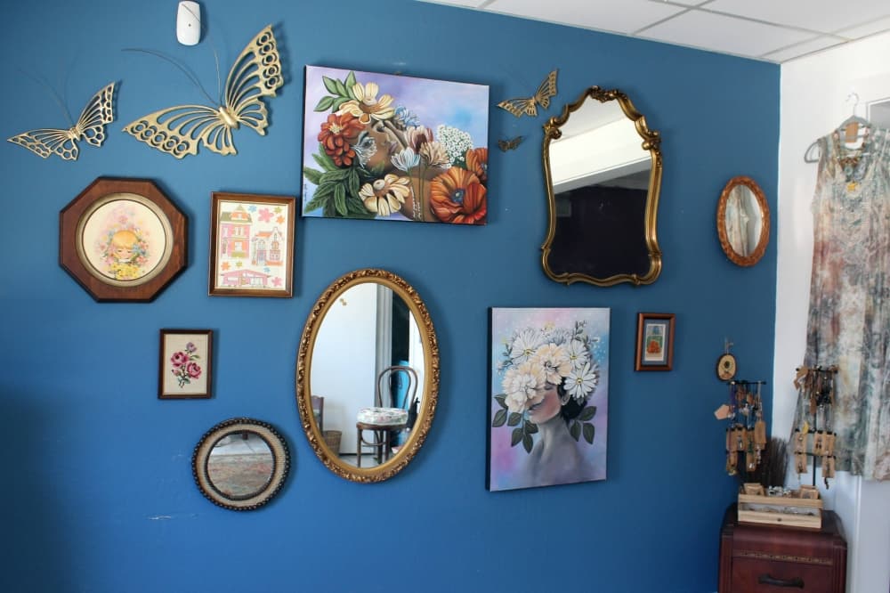 Framed art and needlework displayed on a blue wall. 