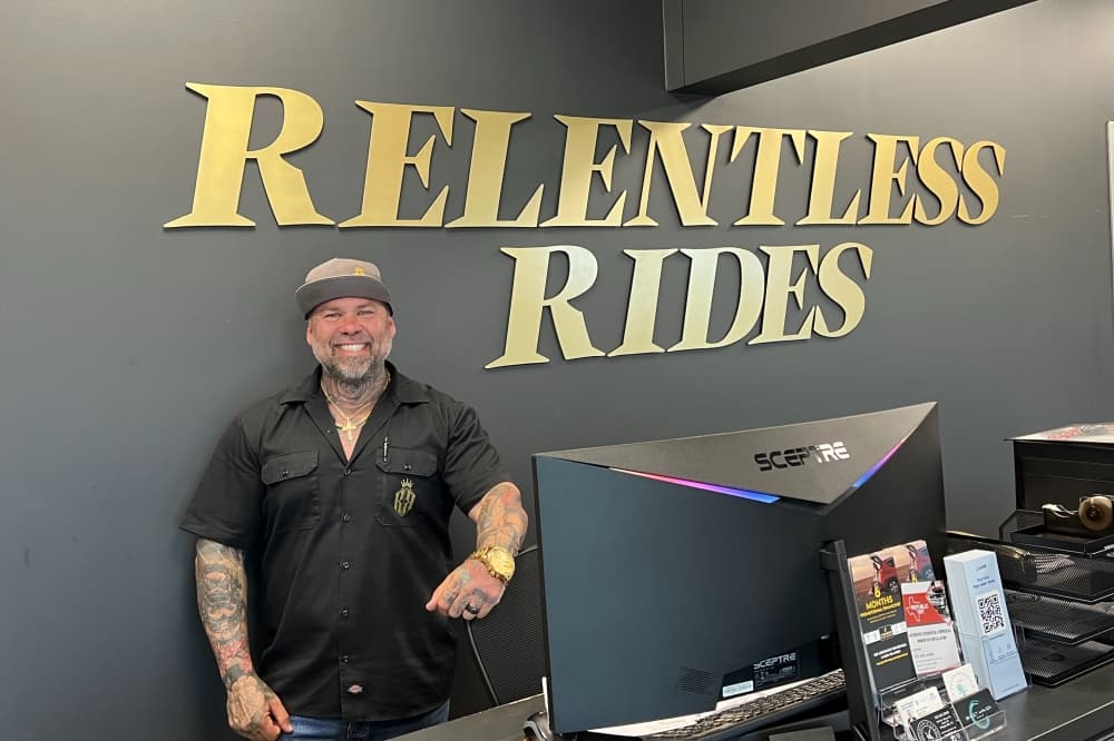 The owner of Relentless Rides stands in front of the sign for the business in its lobby. 