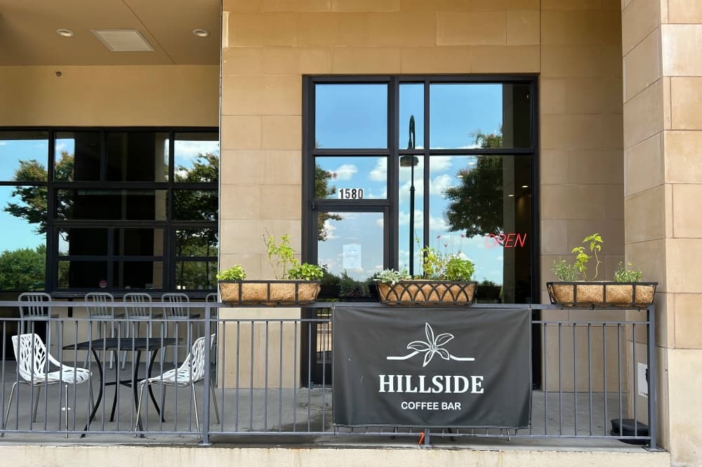 Exterior of patio with Hillside Coffee Bar banner displayed on a short black metal fence. 