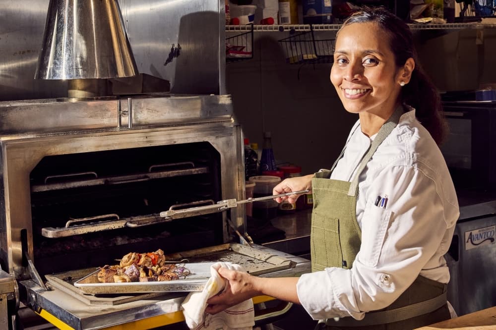 A close up of Lalia Bazahm pulling a dish out of the oven
