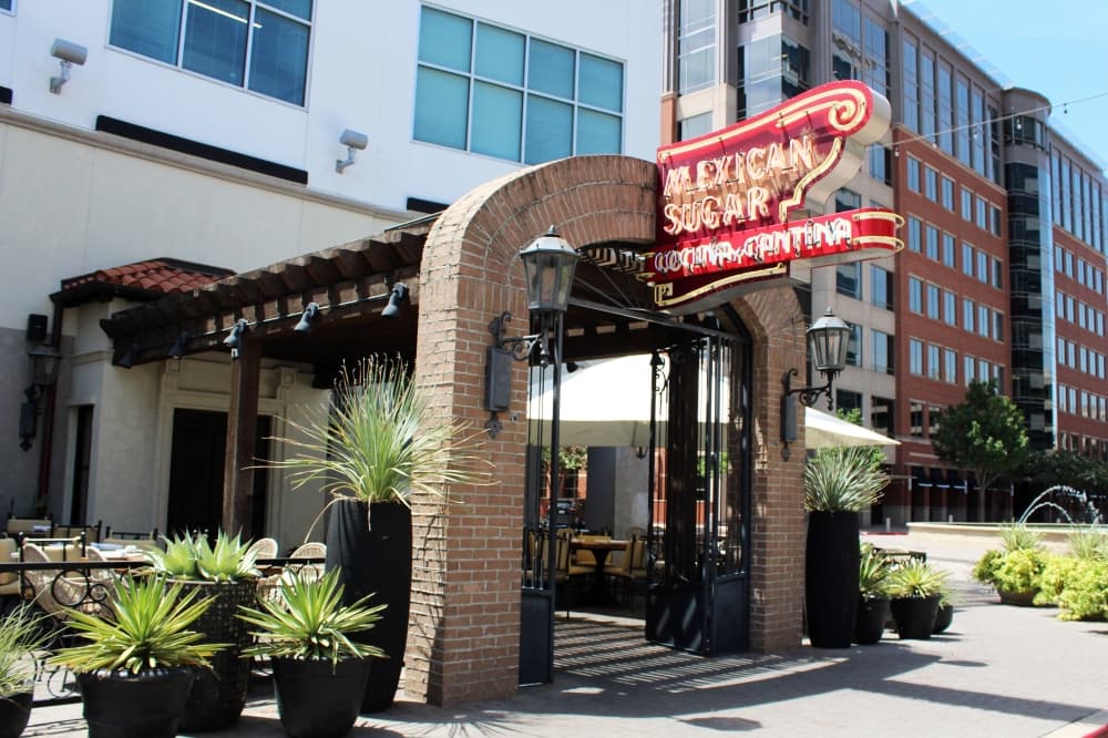 Exterior of a restaurant with Mexican Sugar signage with multi-floored office buildings in the background. 