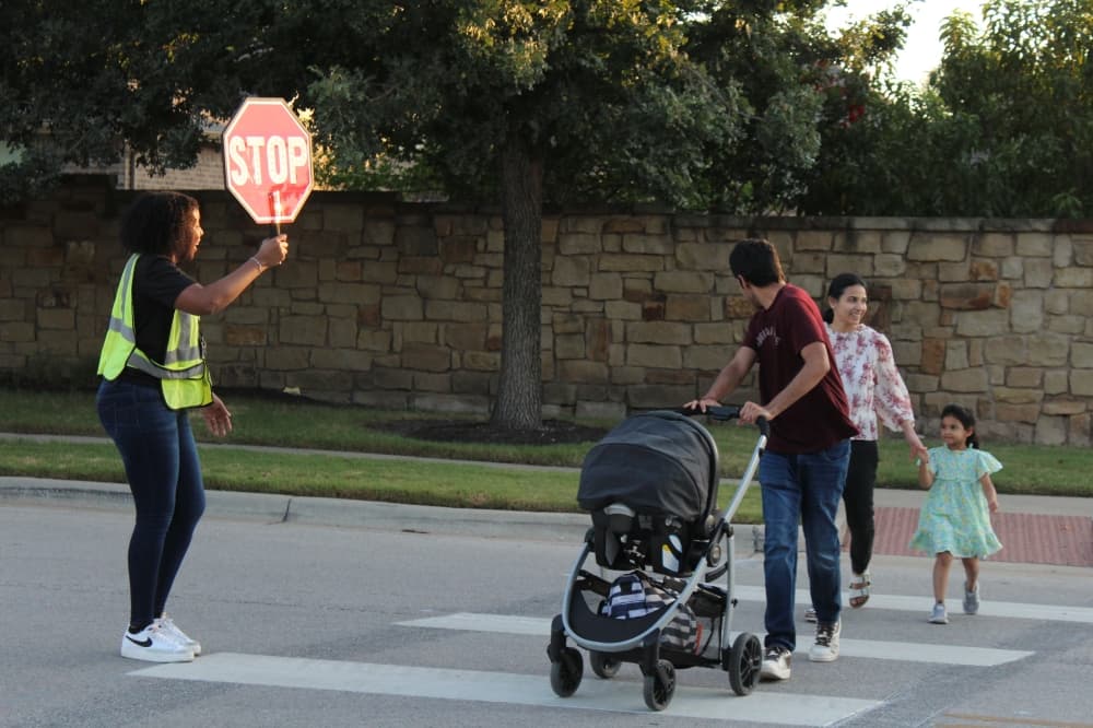 A crossing guard helps control traffic for a family. (Grant Crawford/Community Impact)