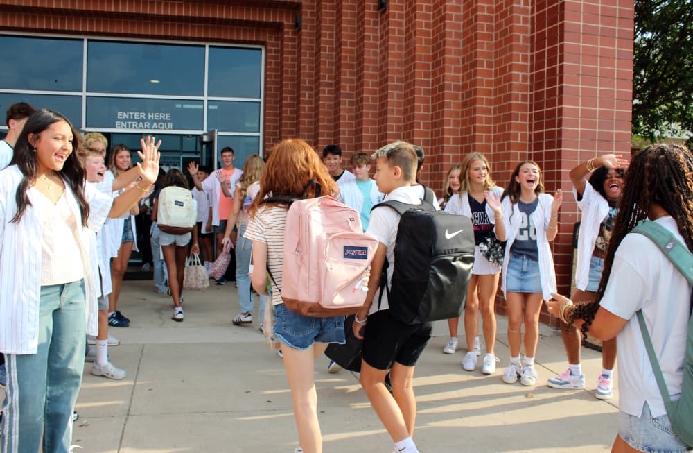Students walking through a line of clapping students facing each other. 