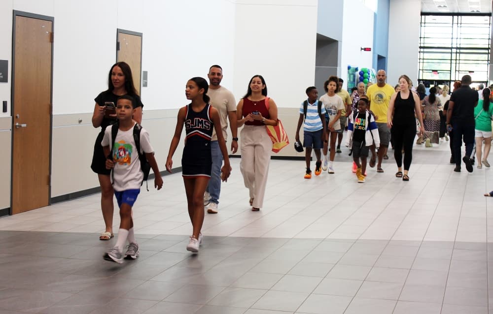 Varying ages of people walking through a school hallway. 