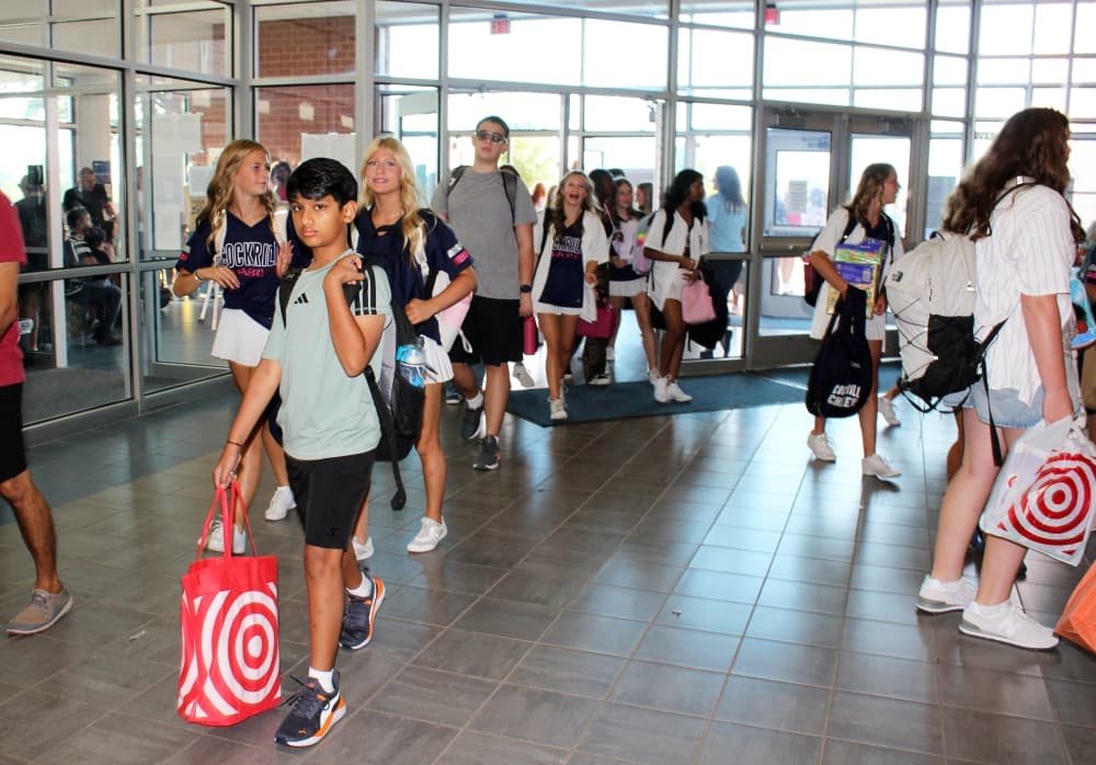 Students walking into school carrying bags and backpacks. 