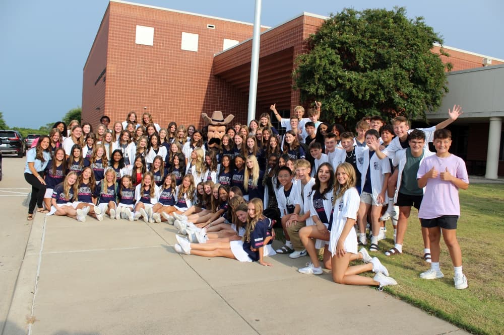 Large group of teens dressed similarly in front of a school .