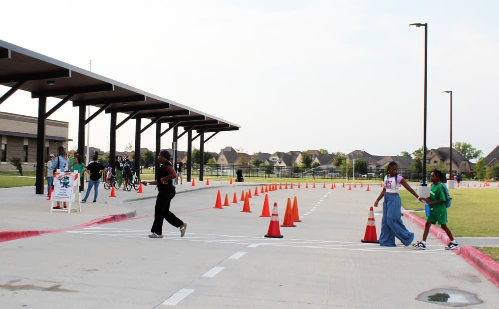 People crossing traffic lanes in front of a school. 