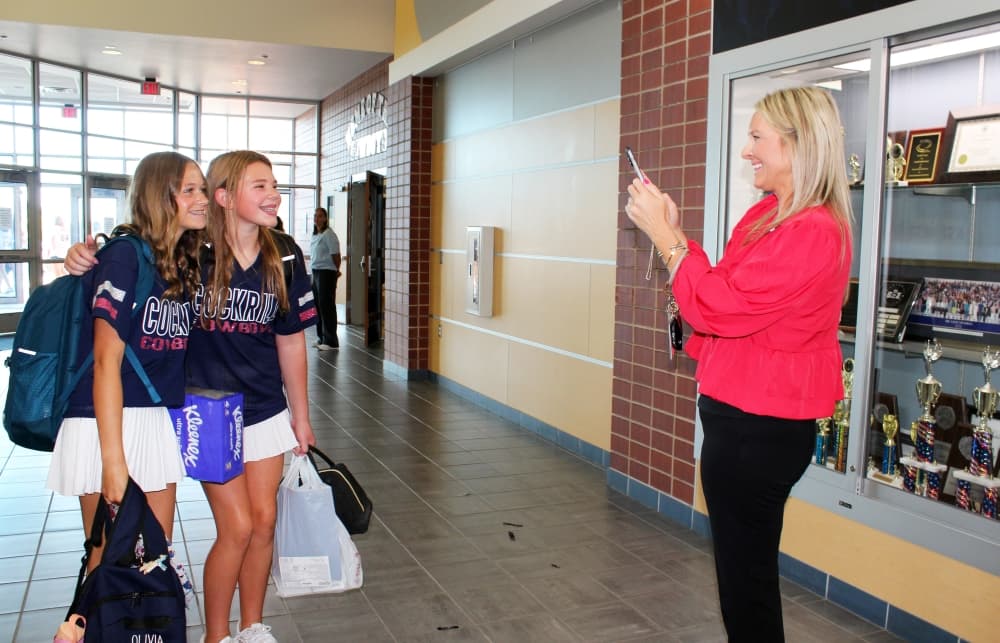 Adult female takes a phone photo of two teen females. 