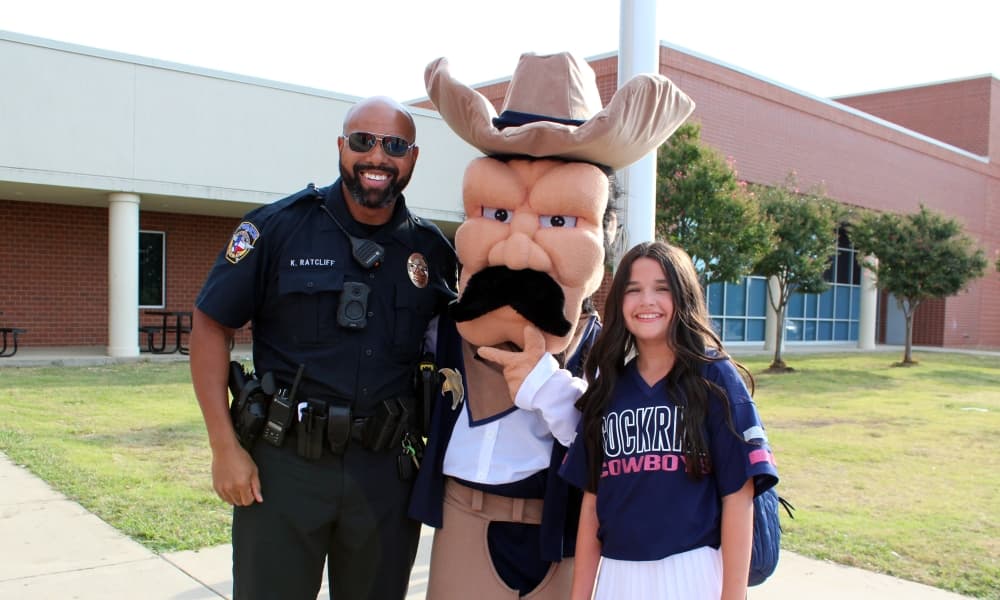 Male officer standing with cowboy mascot and teen girl. 