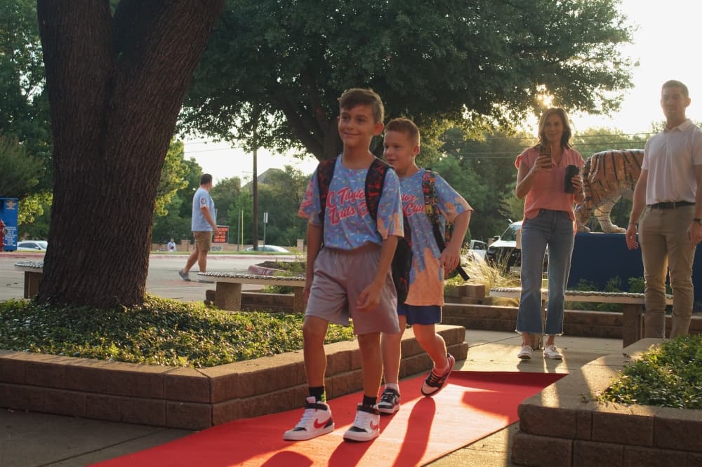 students walk down a red carpet toward school