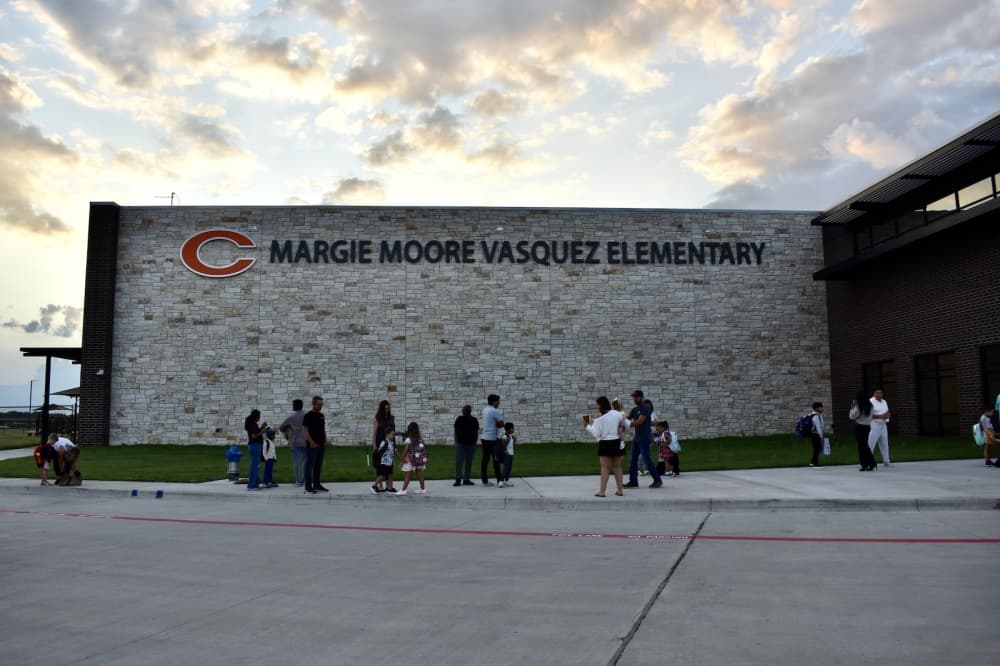 a line of parents and students on a sidewalk outside of an elementary school