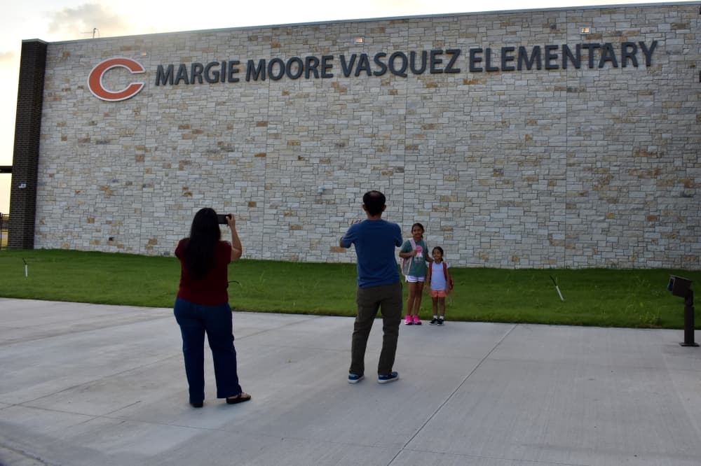 two parents take photos of their children by an elementary school sign
