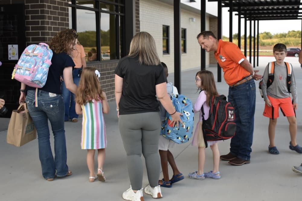 a group of students stop to say hi to adults before walking into school