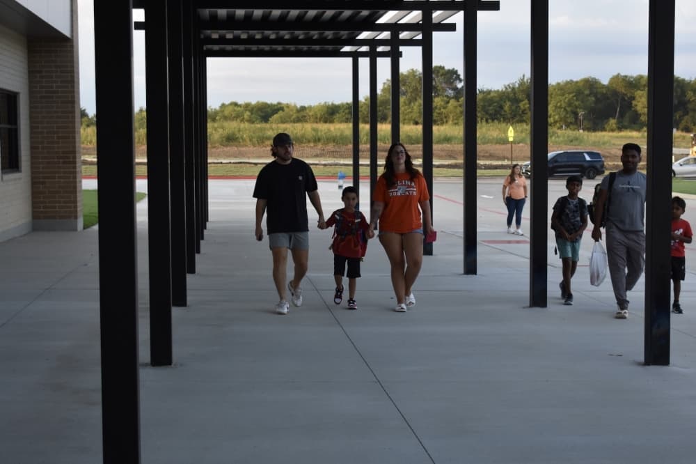 a young child holds his parents hands while walking into school